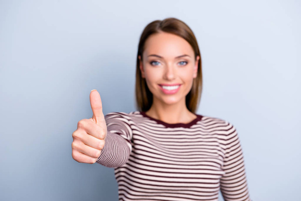 Portrait of nice brunette girl in sweater on blurred grey background showing focised thumb up front to the camera - Foto, Imagen