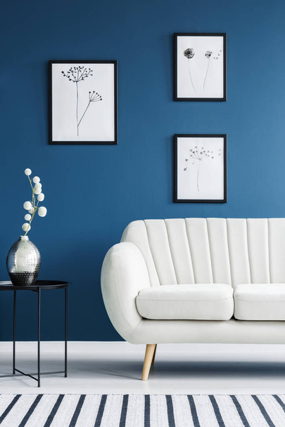 Floral posters, metal side table and white sofa set in a blue living room interior - Foto, imagen