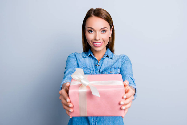 Portrait of cute charming girl presenting a gift in pink packaging with white bow standing over grey background - Foto, Imagen