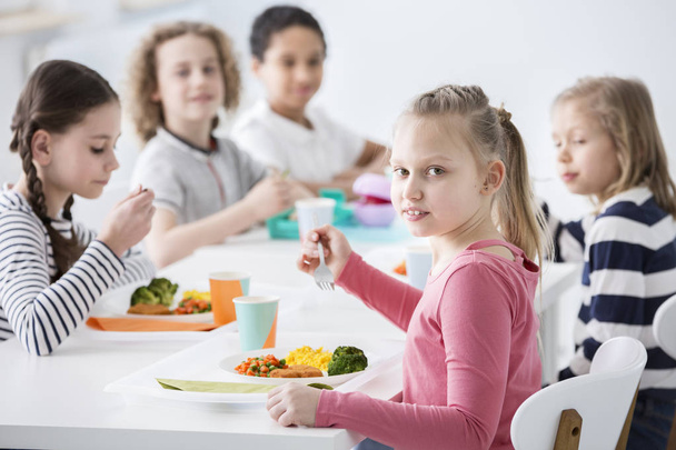 Girl eating vegetables with friends in the canteen during break at school - Foto, Imagen