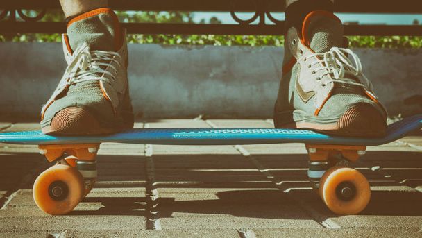 Beine in Vintage-Turnschuhen stehen auf einem Skateboard. Ein Skateboarder ruht auf einer Bank, eine alte künstlerische Tonung. - Foto, Bild