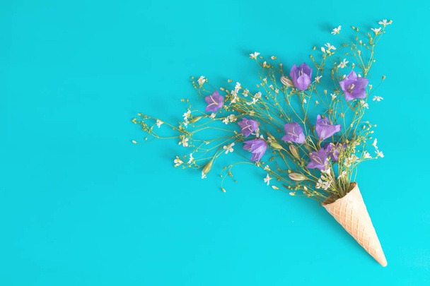 drei Waffelkegel mit blauen Glocken und weißen Blumen blühen Sträuße auf blauer Oberfläche. flache Lage, von oben betrachtet floraler Hintergrund. - Foto, Bild