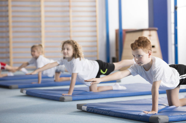 Primary school boy and other kids exercising a balancing table yoga pose during extracurricular gym class to help with posture and core body strength - Fotoğraf, Görsel