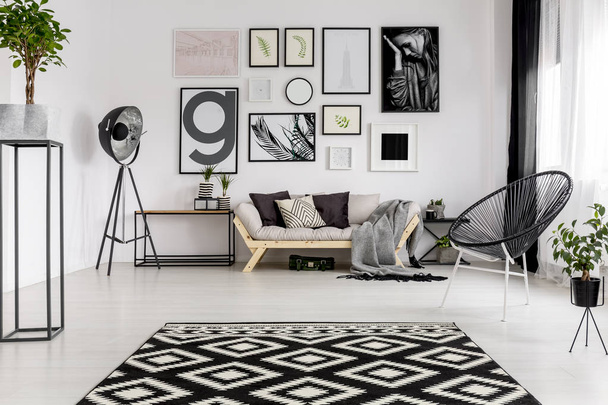 Black and white patterned carpet in modern living room interior with posters and lamp next to sofa - Foto, afbeelding
