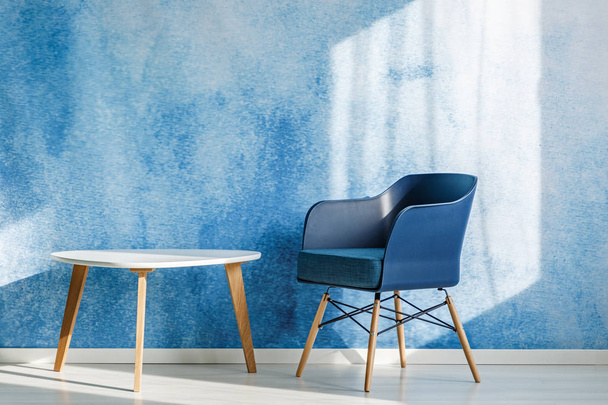 Navy blue armchair next to white wooden table in minimal living room interior - Valokuva, kuva