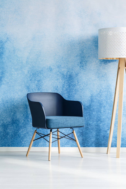 Sillón azul marino junto a lámpara de madera blanca en el interior de la sala de estar moderna con pared de ombre
 - Foto, imagen
