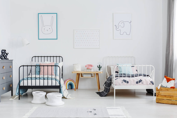 Tavolo in legno tra letto bianco e nero in camera da letto per bambini interno con poster. Foto reale
 - Foto, immagini