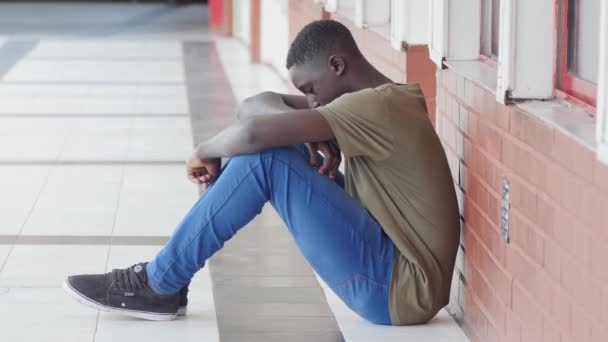 Bullismo scolastico. Afro americano maschio adolescente sconvolto seduto nel corridoio della scuola
. - Filmati, video