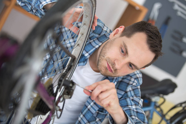closeup photo of young man repairing bicycle rear wheel - Foto, afbeelding
