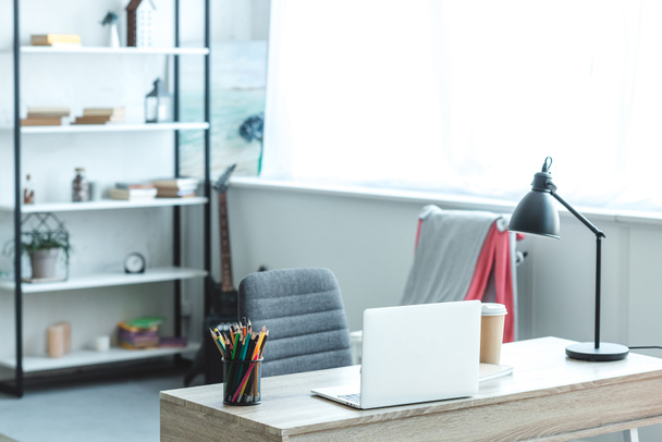 laptop και καφέ για να πάει σε ξύλινο γραφείο στο άνετο δωμάτιο με μοντέρνα διακόσμηση - Φωτογραφία, εικόνα