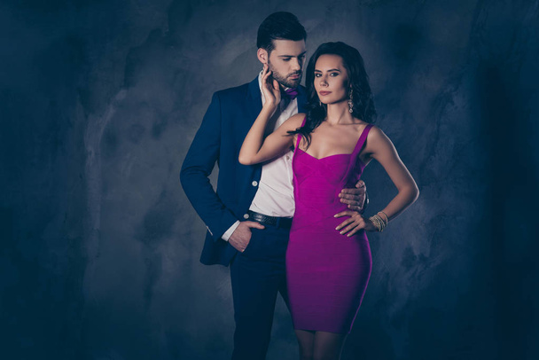 Portrait of naughty man in tuxedo embracing his tempting hispanic latin woman in tight dress with decollete hairstyle, attractive dreamy couple isolated on grey background with copy space - Photo, image