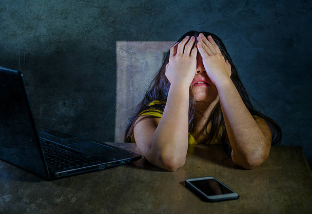 dramatyczne portret Młoda Łacińskiej smutny i przestraszony kobieta obejmujących twarz rękami zdesperowany i depresji z laptopa i telefonu komórkowego w cyber zastraszanie i internet problem  - Zdjęcie, obraz