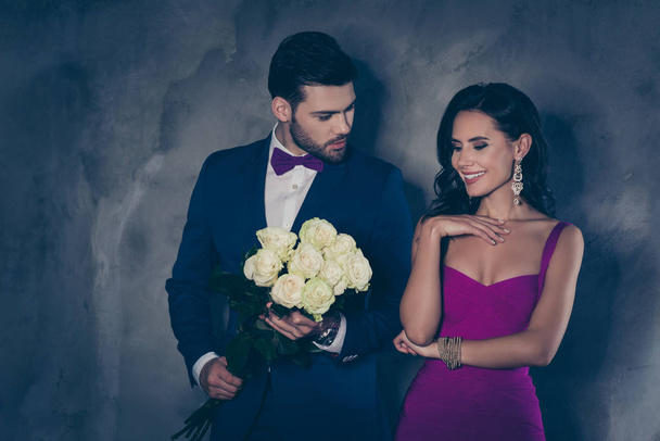 Portrait of charming mrs in dress decollete attractive mr in tuxedo with bow holding bouquet of white roses prepare surprise, lovely romantic spouses isolated on grey background. Wedding special day - Valokuva, kuva