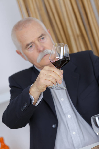 satisfied mature man holds a red wine glass - Фото, изображение