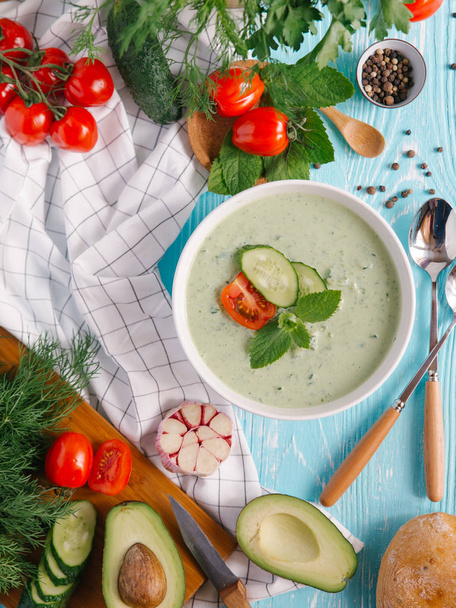 Bowl with cream of avocado soup with tomatoes and cucumbers on blue wooden background - Foto, immagini