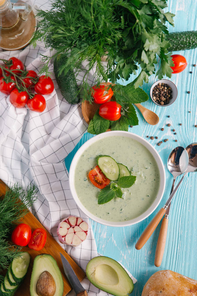 Tál krém avokádó leves, paradicsom és uborka, kék fa háttér - Fotó, kép