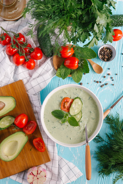 Bowl with cream of avocado soup with tomatoes and cucumbers on blue wooden background - Photo, Image