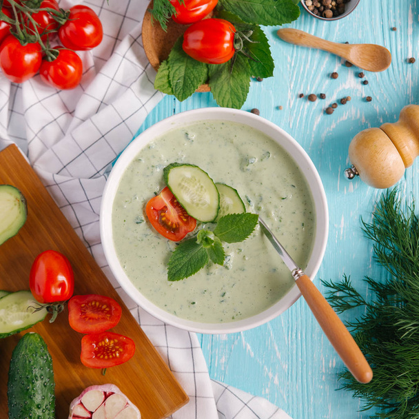 Kom met de crème van avocado soep met tomaten en komkommers op blauwe houten achtergrond - Foto, afbeelding