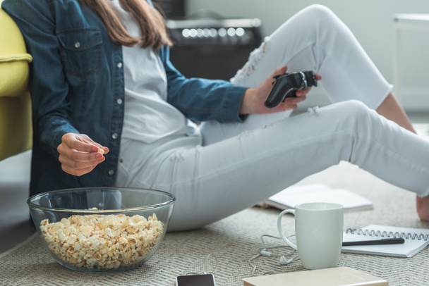 Schnappschuss von Mädchen, das Popcorn isst und zu Hause mit Joystick spielt - Foto, Bild