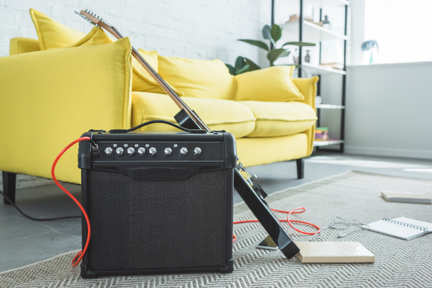 electric guitar and loud speaker standing on floor with books near sofa - Foto, Imagem