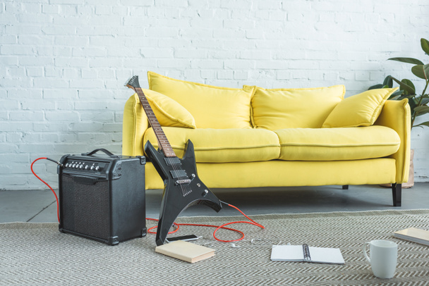electric guitar, loud speaker, smartphone, books and cup of coffee on floor near yellow sofa in living room - Photo, Image