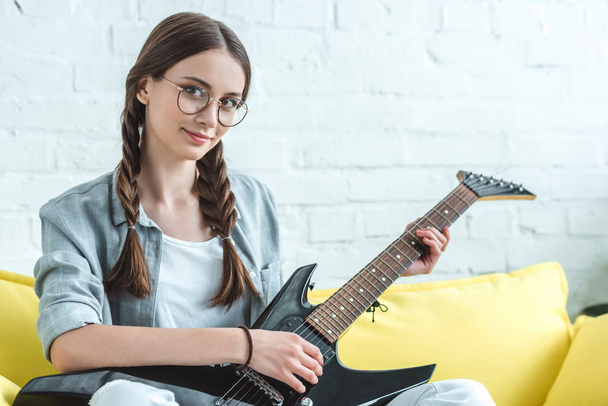 attractive female teenager playing electric guitar on sofa at home  - Fotó, kép