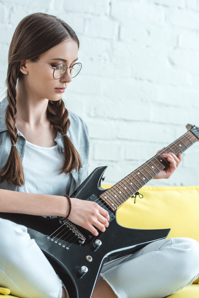 attractive teen girl playing black electric guitar on sofa - Foto, imagen