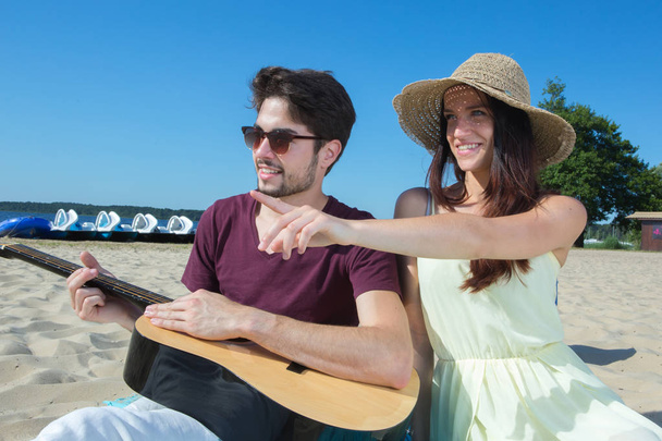 young man with his guitar and girlfriend on the beach - Фото, изображение