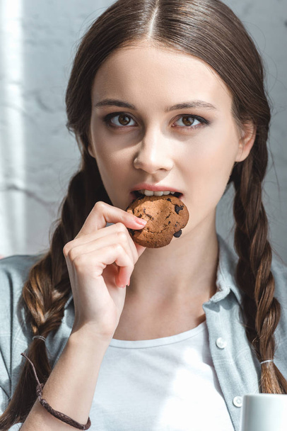 beautiful teen girl eating cookie and looking at camera - Zdjęcie, obraz