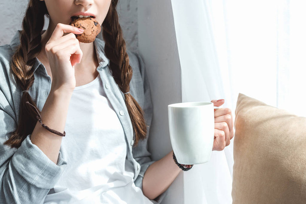 cropped view of girl eating cookie and drinking coffee - Photo, Image