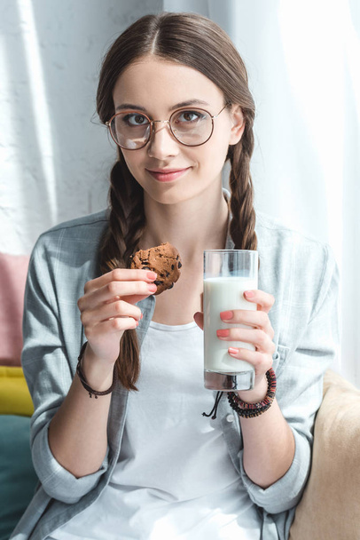 mooie tiener meisje met cookie en melk in glas - Foto, afbeelding