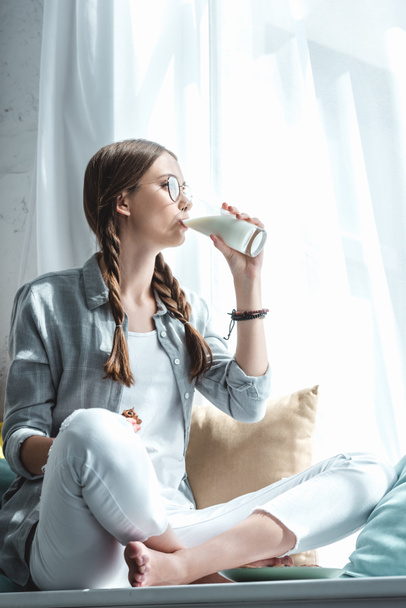 beautiful girl eating cookies and drinking milk on windowsill - Zdjęcie, obraz