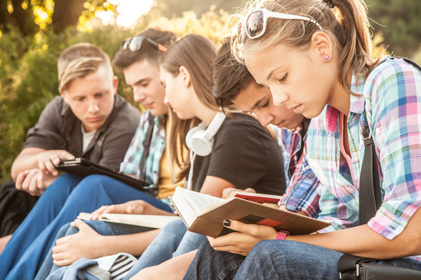 grupo de jóvenes estudiantes con libros y artilugios se sientan en los escalones del parque
 - Foto, Imagen