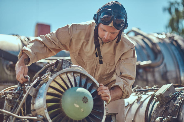 Portrait d'un pilote mécanicien en uniforme et casque volant, réparant la turbine d'avion démontée dans un musée en plein air
. - Photo, image
