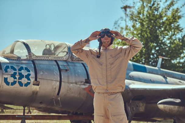 Mecánico en uniforme y casco volador de pie cerca de un viejo caza-interceptor de guerra en un museo al aire libre
. - Foto, Imagen