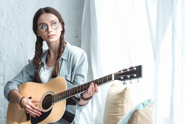 όμορφο κορίτσι παίζει ακουστική κιθάρα κοντά σε παράθυρο - Φωτογραφία, εικόνα