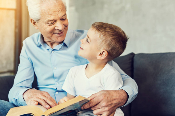 Caring grandfather reading a book to his grandson - Фото, изображение