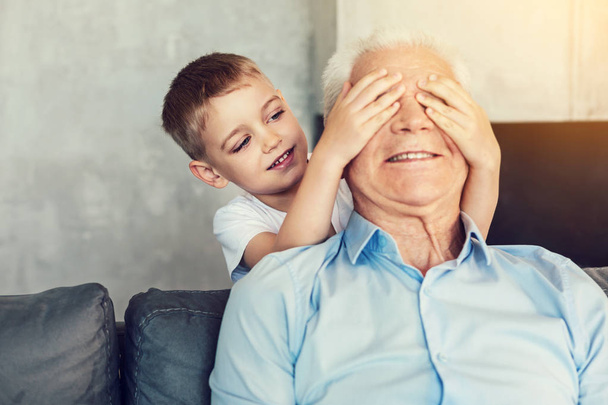 Funny little boy closing the eyes of his grandpa - Foto, Imagen