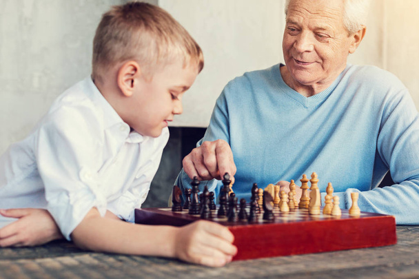 Attentive pensioner playing chess with a little boy - 写真・画像