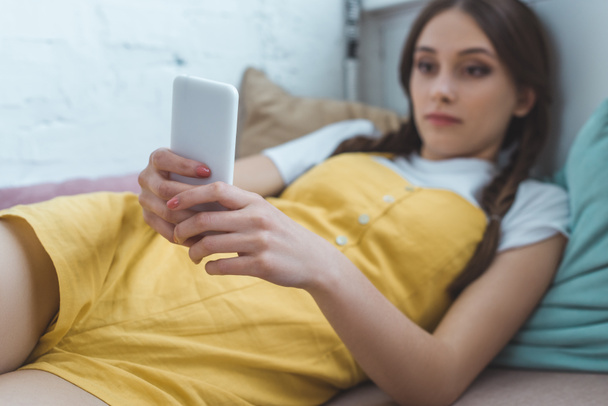 selective focus of teen girl using smartphone and lying on sofa - Zdjęcie, obraz