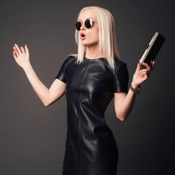 verbaasd stijlvolle vrouw in zwart leer jurk met zilveren zakje en horloge. Fashion concept. - Foto, afbeelding