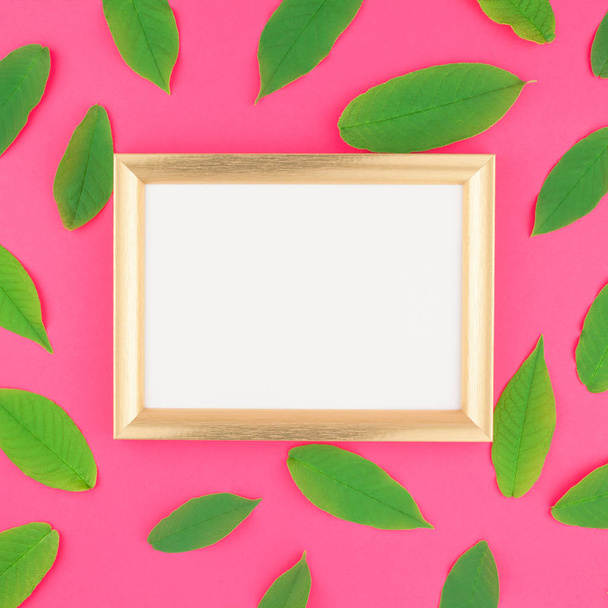 Creative flat lay top view pattern with fresh green leaves on bright pink square background with golden frame mock up and copy space in minimal pop art style, template for text - Foto, afbeelding