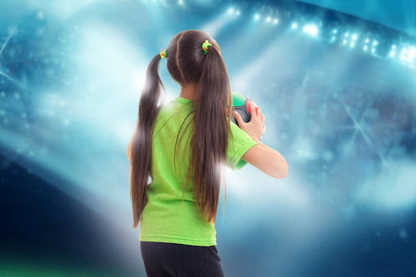little girl in green shirt with soccer ball in hands on football stadium - Zdjęcie, obraz