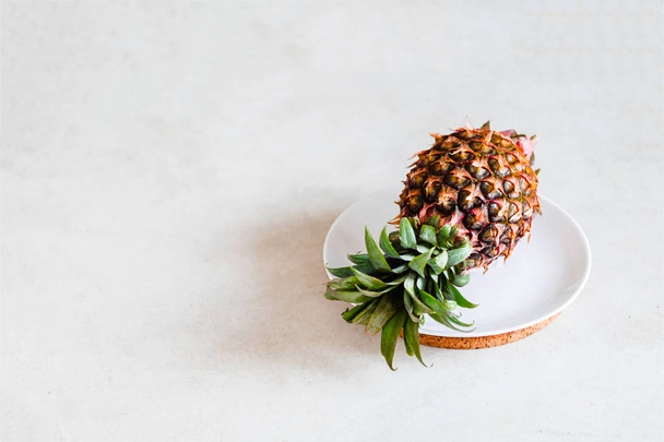 Pineapple on a white plate, gray concrete background. Creative layout, minimal food photography concept. Copyspace, horizontal - Zdjęcie, obraz