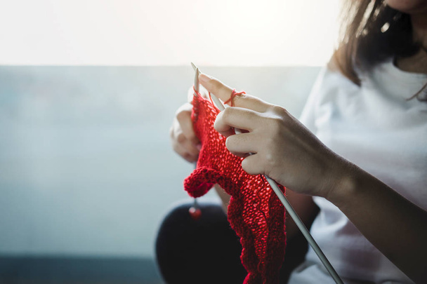 Close up shot of young woman hands knitting a red scarf handicraft in the living room on terrace at home. - Fotografie, Obrázek