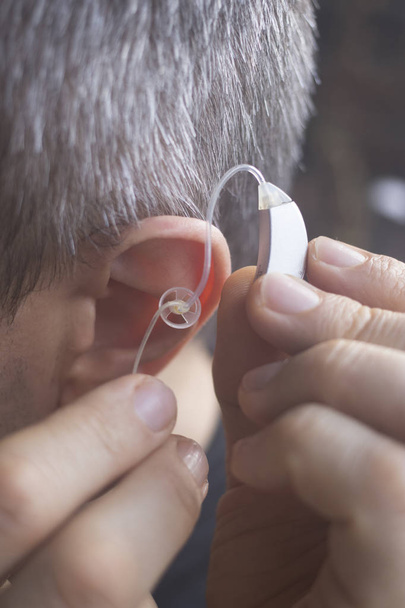聴覚障害者の中年男の耳で身に着けている現代デジタル高技術補聴器. - 写真・画像