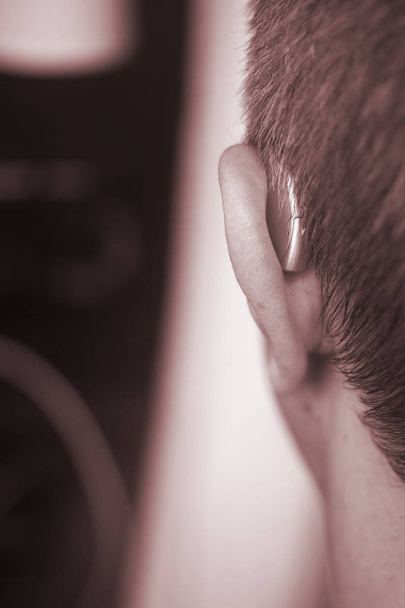 Deaf middle aged man wearing modern digital high technology hearing aid in ear. - Фото, изображение