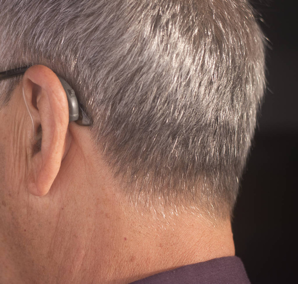 Kuuro eläkeläinen mies yllään moderni digitaalinen korkean teknologian kuulolaite korvaan
. - Valokuva, kuva
