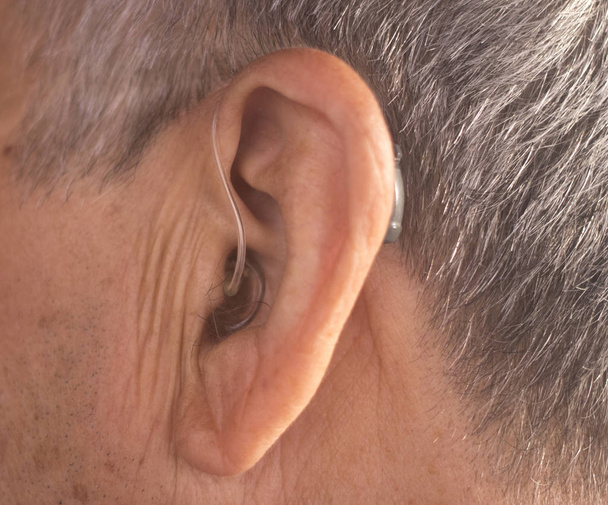 Deaf senior citizen man wearing modern digital high technology hearing aid in ear. - Photo, Image