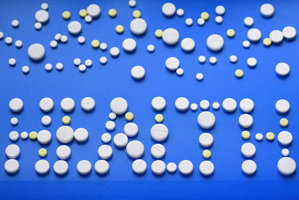 Comprimidos amarillos y blancos esparcidos en una mesa médica azul, fondo, salud de la inscripción
 - Foto, imagen